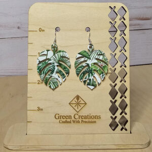 Tropical monstera leaf acrylic earrings with green foliage pattern on wooden display stand.