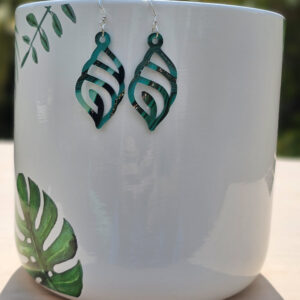 Green marbled swirl leaf earrings hanging on a white ceramic planter with tropical leaf illustrations.