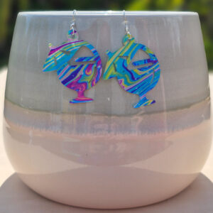 Bright cocktail glass earrings with umbrella detail hanging on a ceramic pot in sunlight.